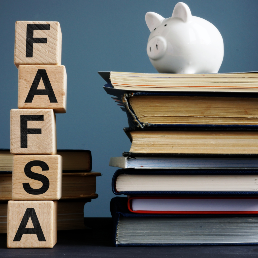 A stack of books with a white piggy bank on top and on the left a stack of wooden blocks that spell "FAFSA"