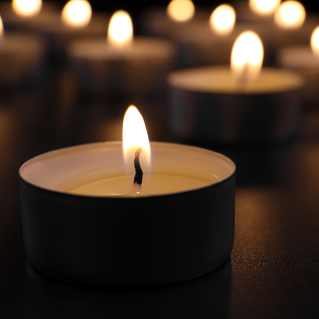 A lit tea candle with several lit candles in the background